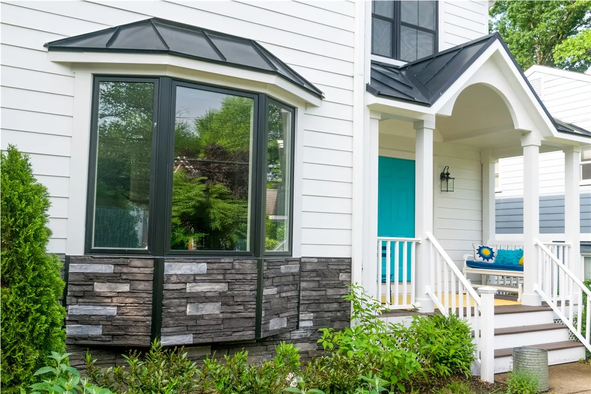A black-framed bay window installed by Alco Products on a white-sided home with a stone base