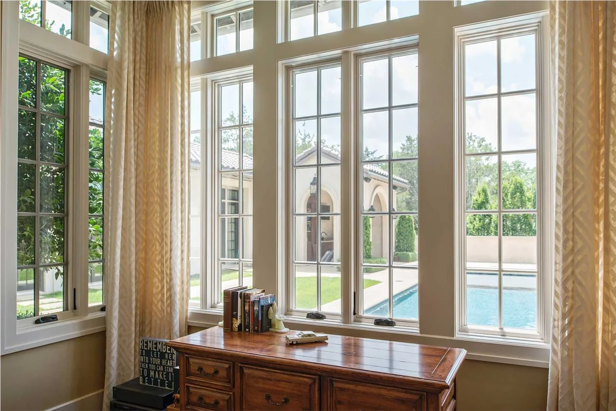 A wall of tall Marvin windows in a home office overlooking a pool