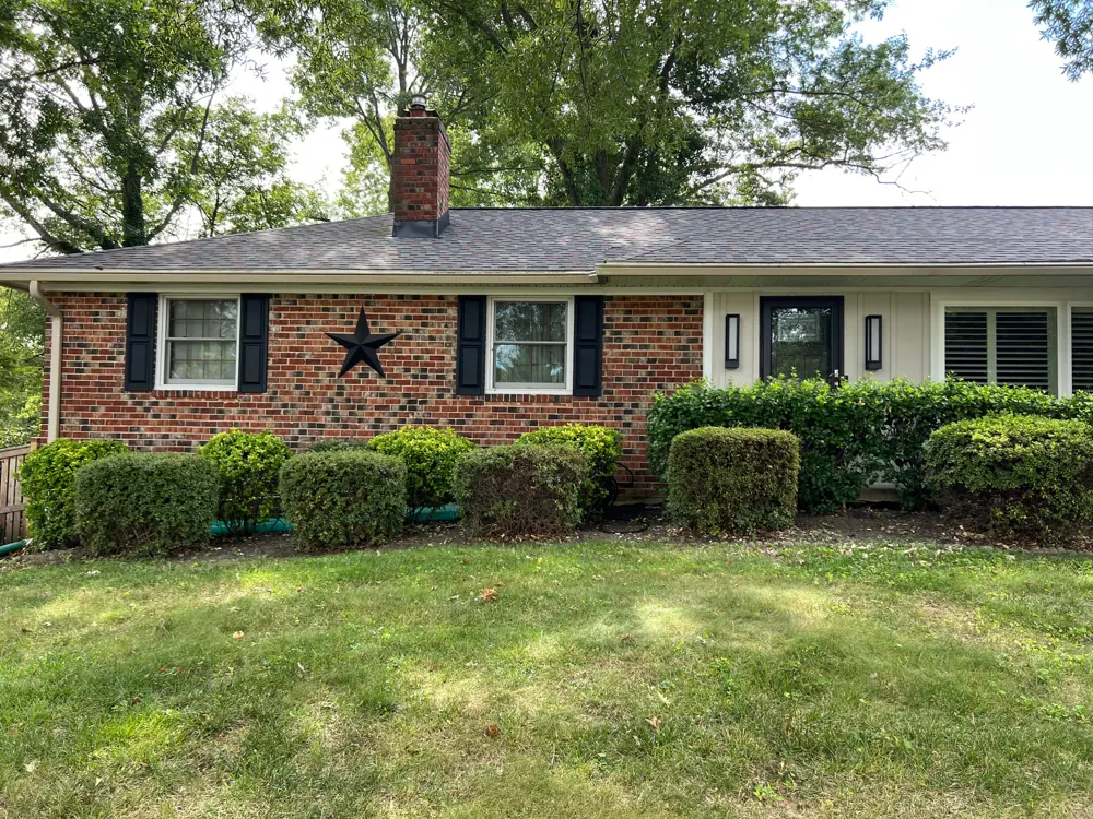 A brick ranch house with black shutters and a new board-and-batten section with a new front door