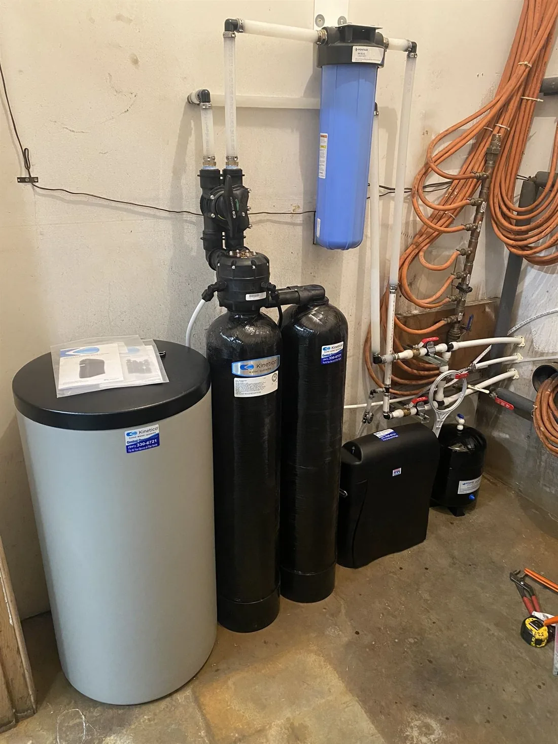 A Kinetico twin-tank softener and brine tank installed against a basement utility wall
