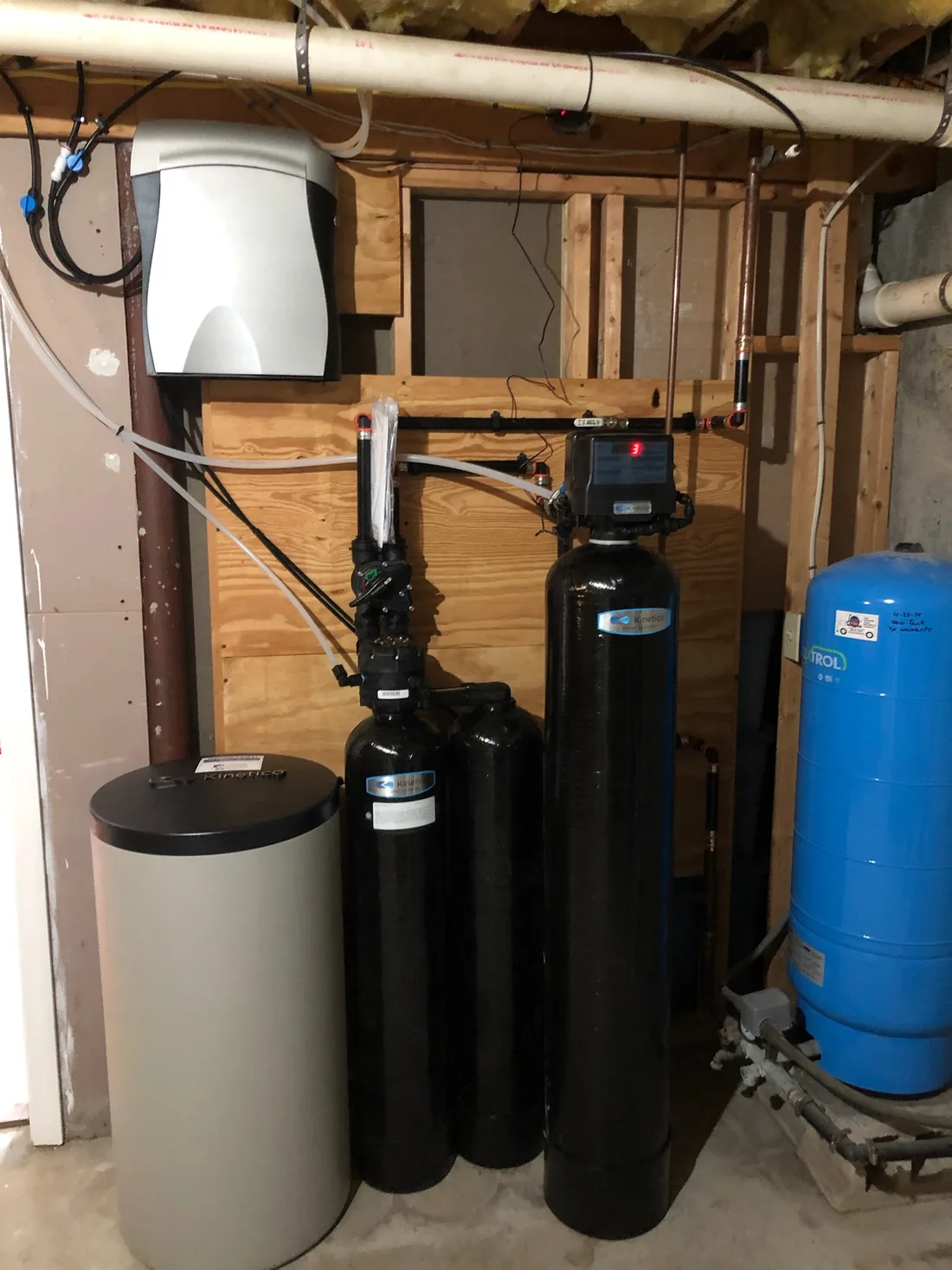 A whole-home filtration and softening system with a blue filter housing, installed in a basement