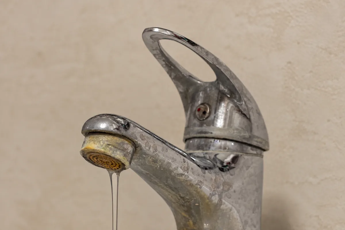 A chrome bathroom faucet spotted with white mineral residue, its aerator crusted over